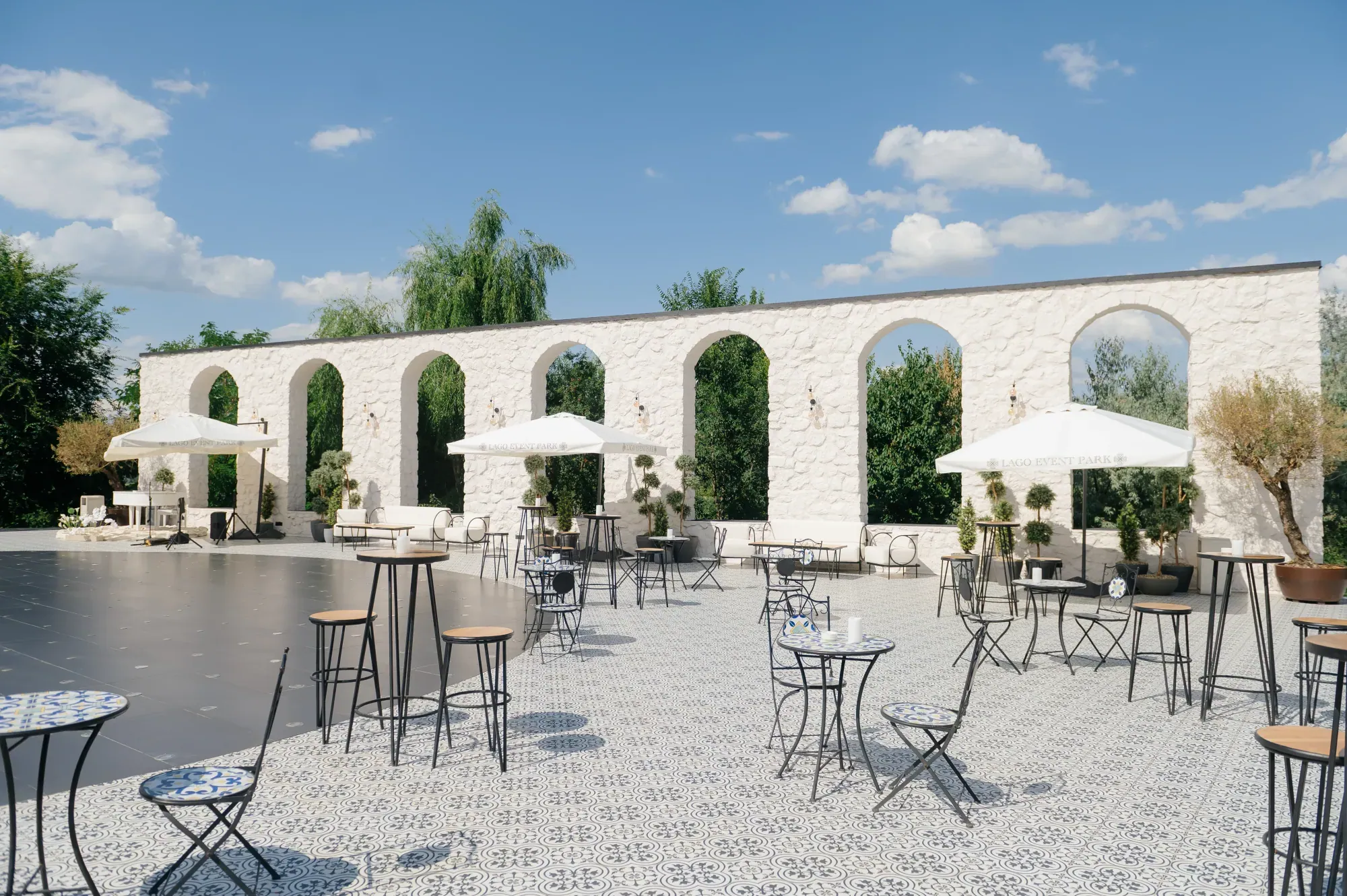 Curtea Lago Event Park, cu arcade din piatră albă, umbrele și mese înalte
