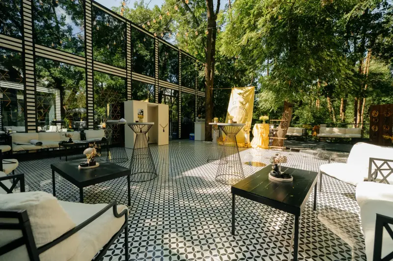 Terasa Villa Garden printre copacii parcului, cu canapele albe și mese de cocktail